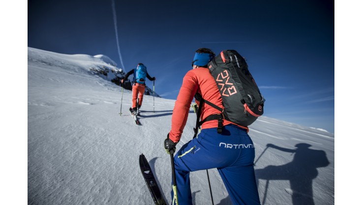 Skiløper som vandrer oppover fjellet med Avabag-skredsekken fra Ortovox