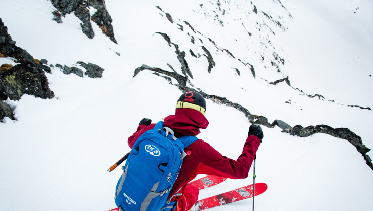 Freeride-skiløper som kjører ned et fjell med en skredsekk av BCA