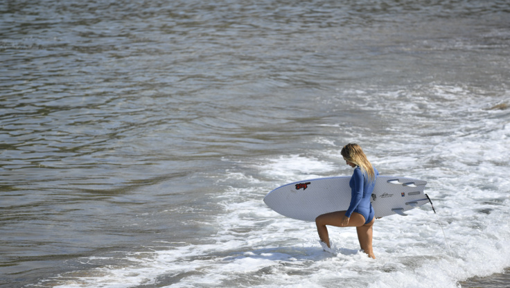 Girl surfer going in the water in a 1 mm springsuit