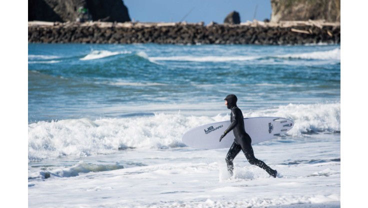 Ein Surfer läuft ins Meer mit einen Langen Neo, Haube, Handschuhe und Schuhe
