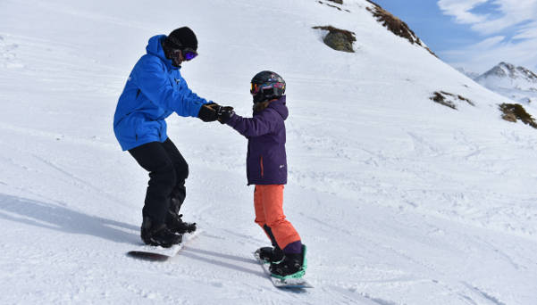 Snowboard teacher helping the pupil with first sliding exercise