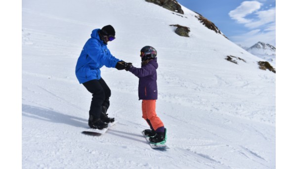 Snowboard teacher helping the pupil with first sliding exercise