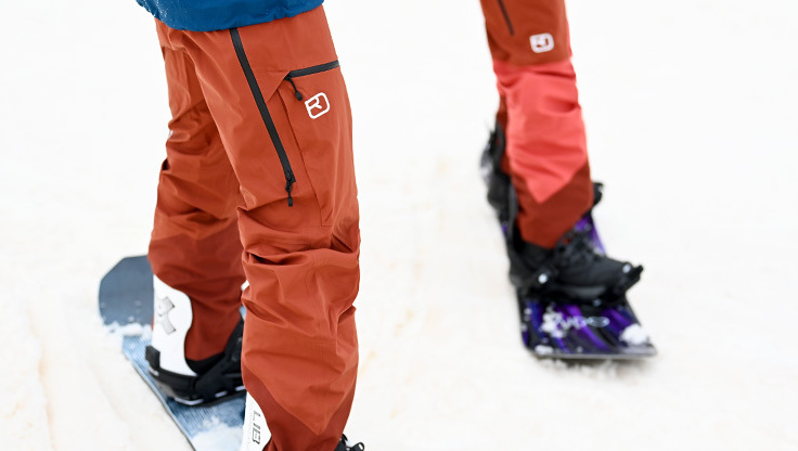 En snowboarder står i sneen i bib-bukser