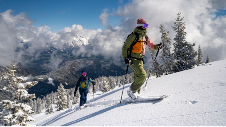 A snowboarder stands at the summit wearing a shell jacket.