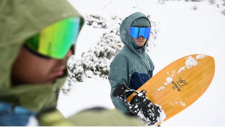 Uno snowboarder si trova sulla cima indossando una giacca a guscio.
