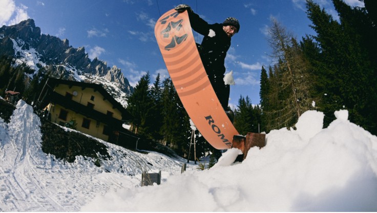 Snowboarder esegue un trick su un box allo snowpark, con una tavola morbida.