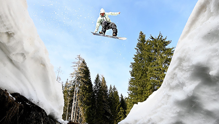 Snowboarder jumping in the powder between the trees with his medium-flex Lib Tech snowboard