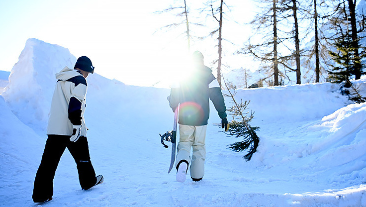 Two snowboarders walking with their snowboard in hand