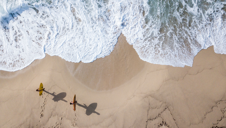 Due principianti che trasportano le loro tavole da surf in spiaggia