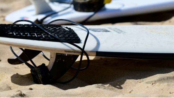 Un ragazzo in spiaggia mentre trasporta la sua tavola, sulla quale ha applicato un traction pad.